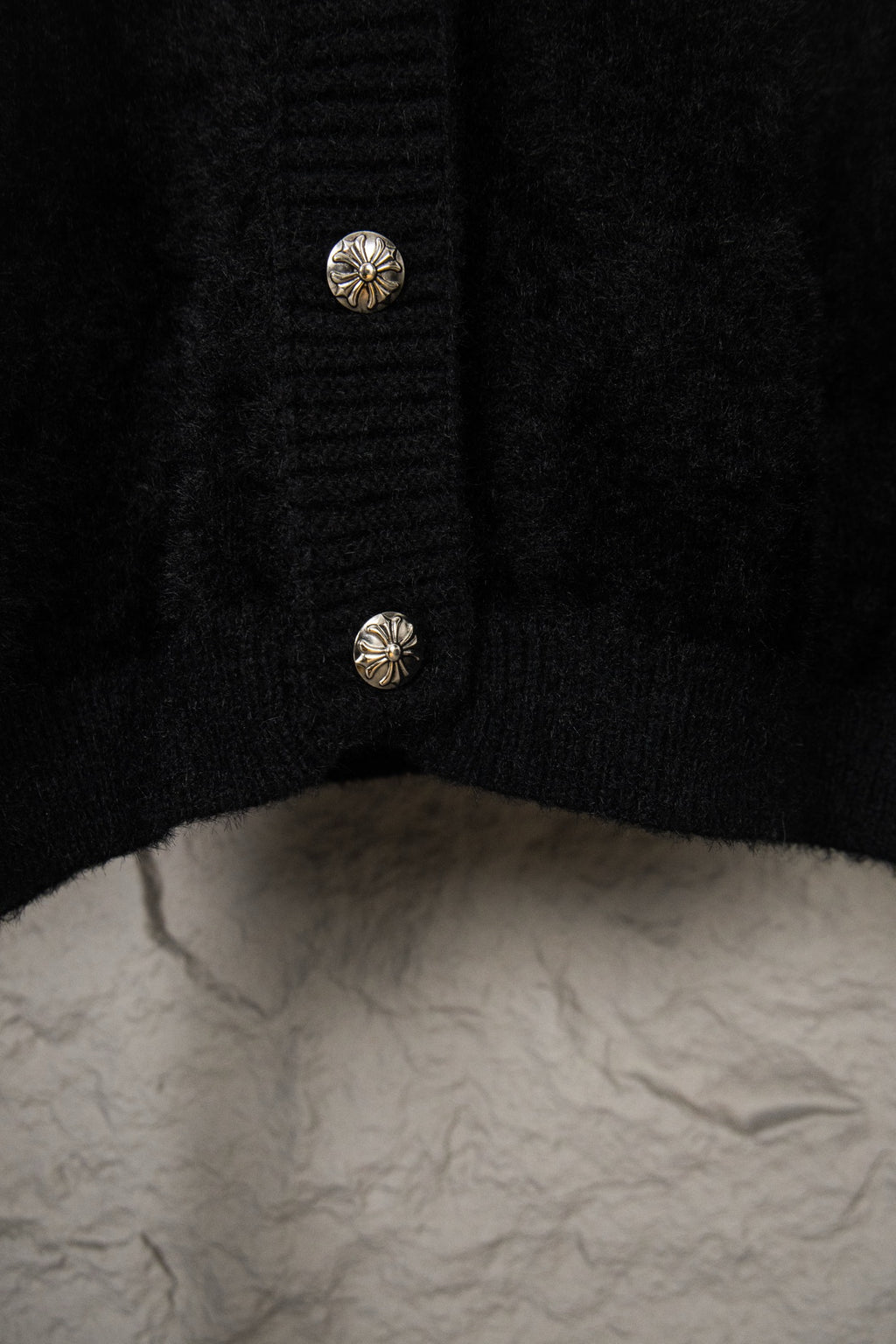 Black cardigan hem close-up with two small silver buttons