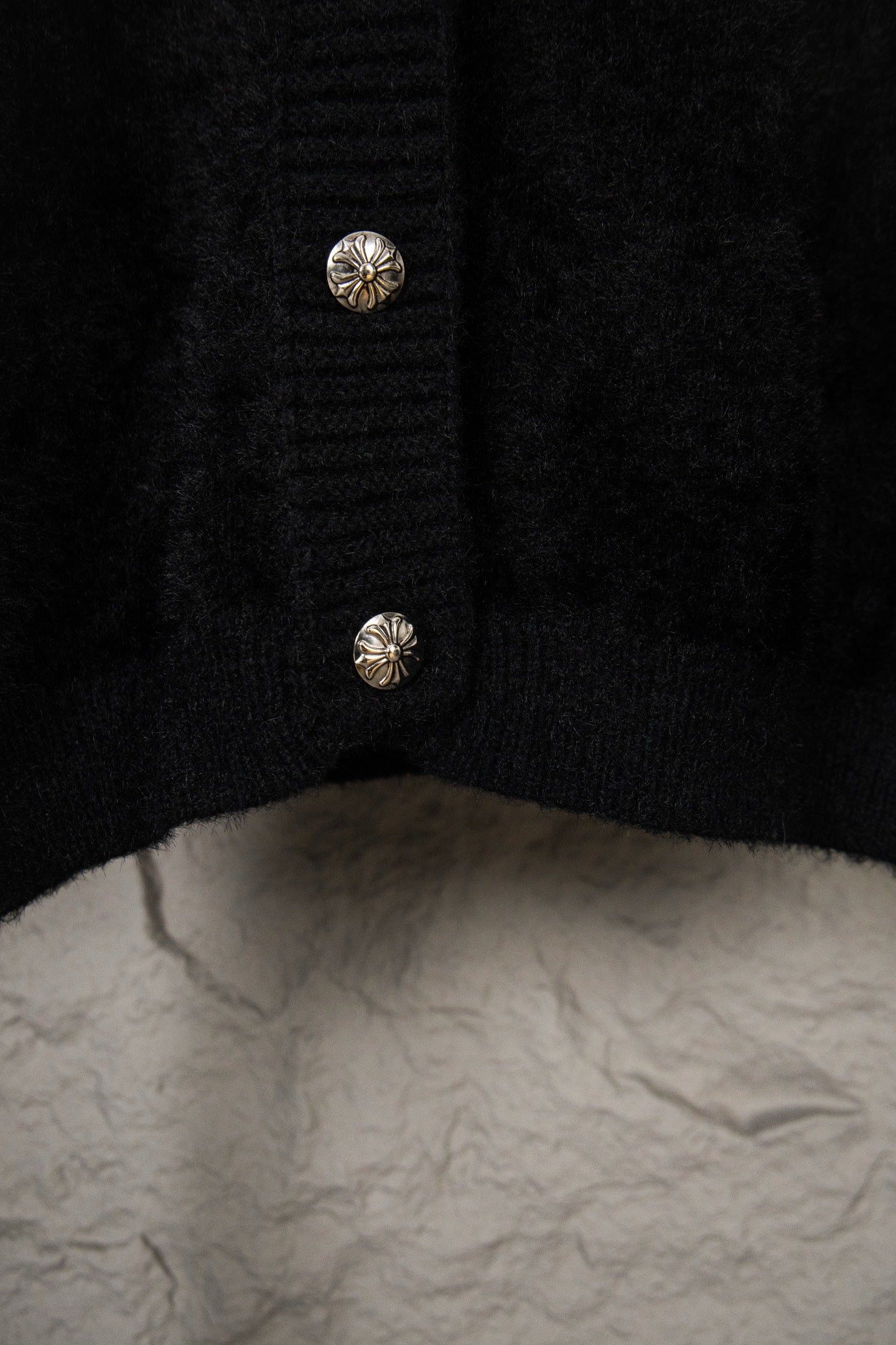 Black cardigan hem close-up with two small silver buttons