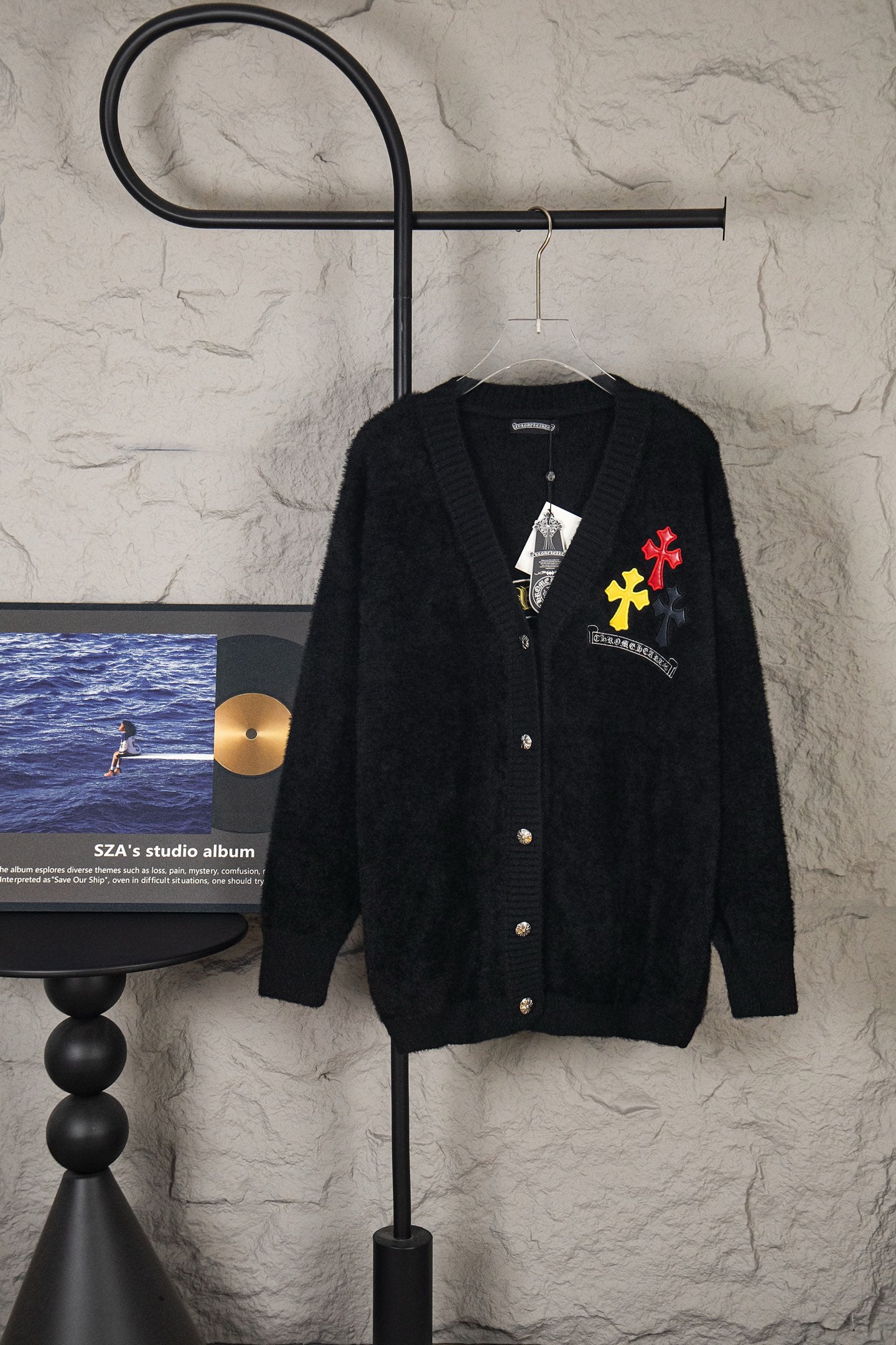Black cardigan sweater on hanger with front buttons and colorful chest patches