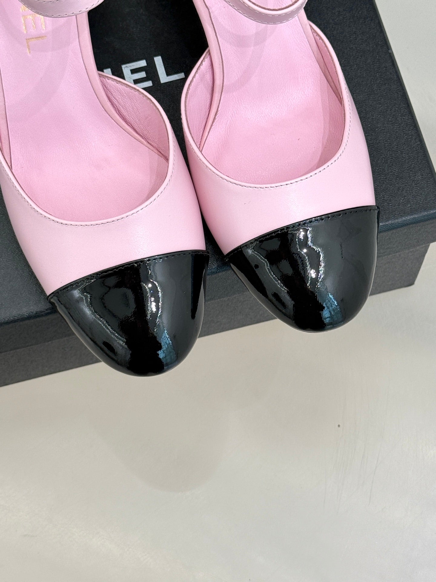 Close-up of pink leather flats with black glossy toe cap and ankle strap