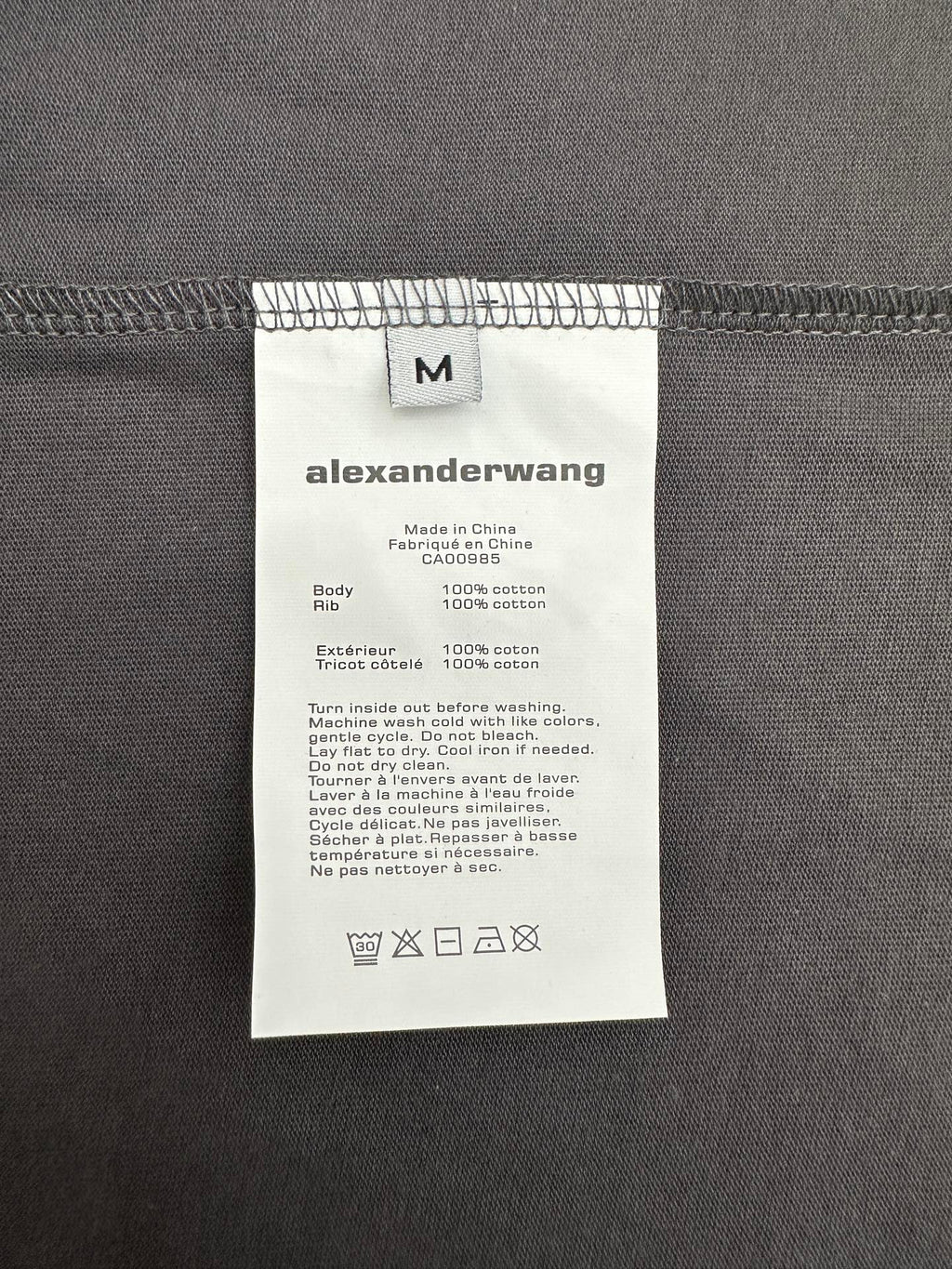 T-shirt care label on dark gray fabric with size and fabric info
