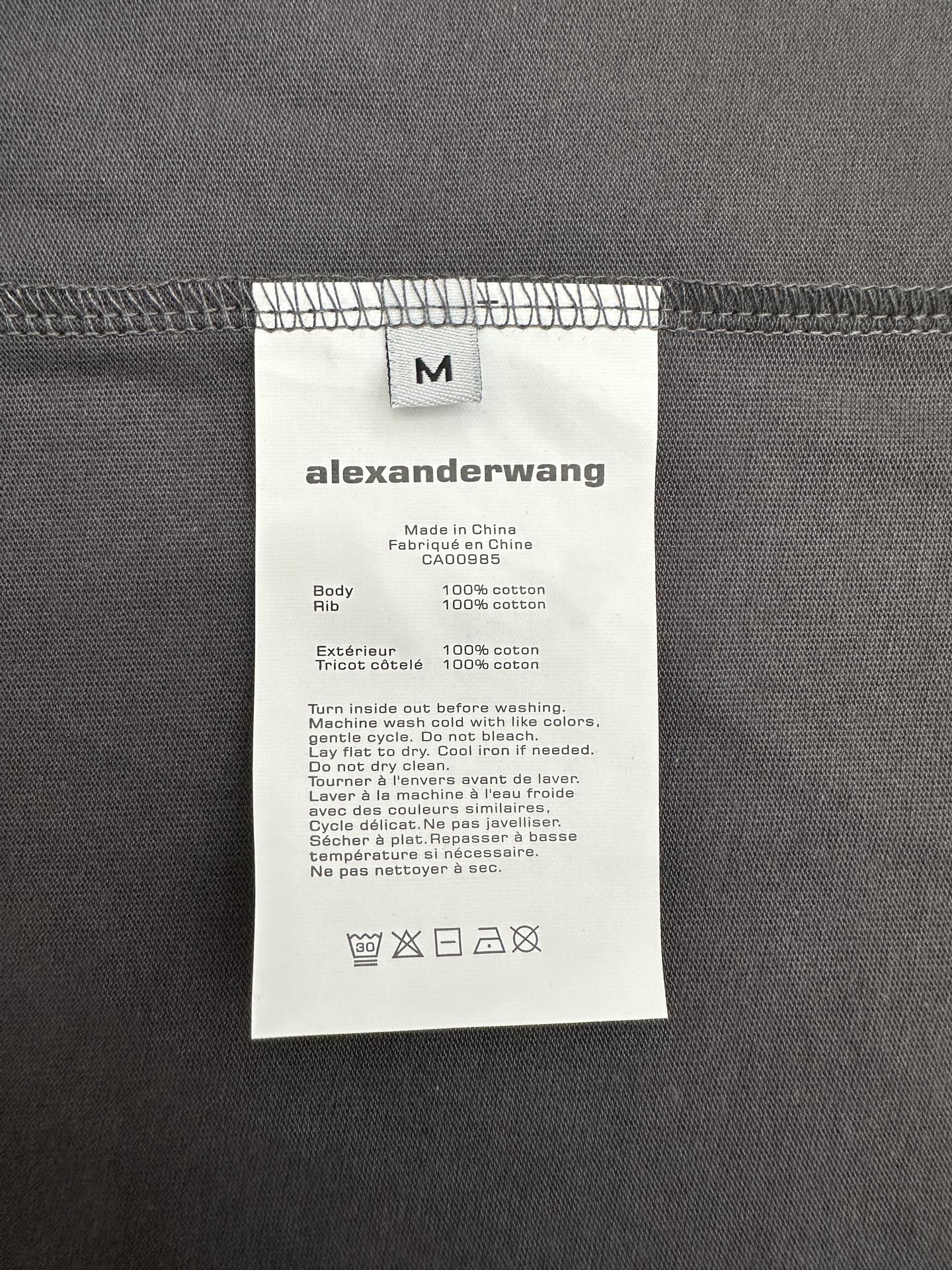 T-shirt care label on dark gray fabric with size and fabric info
