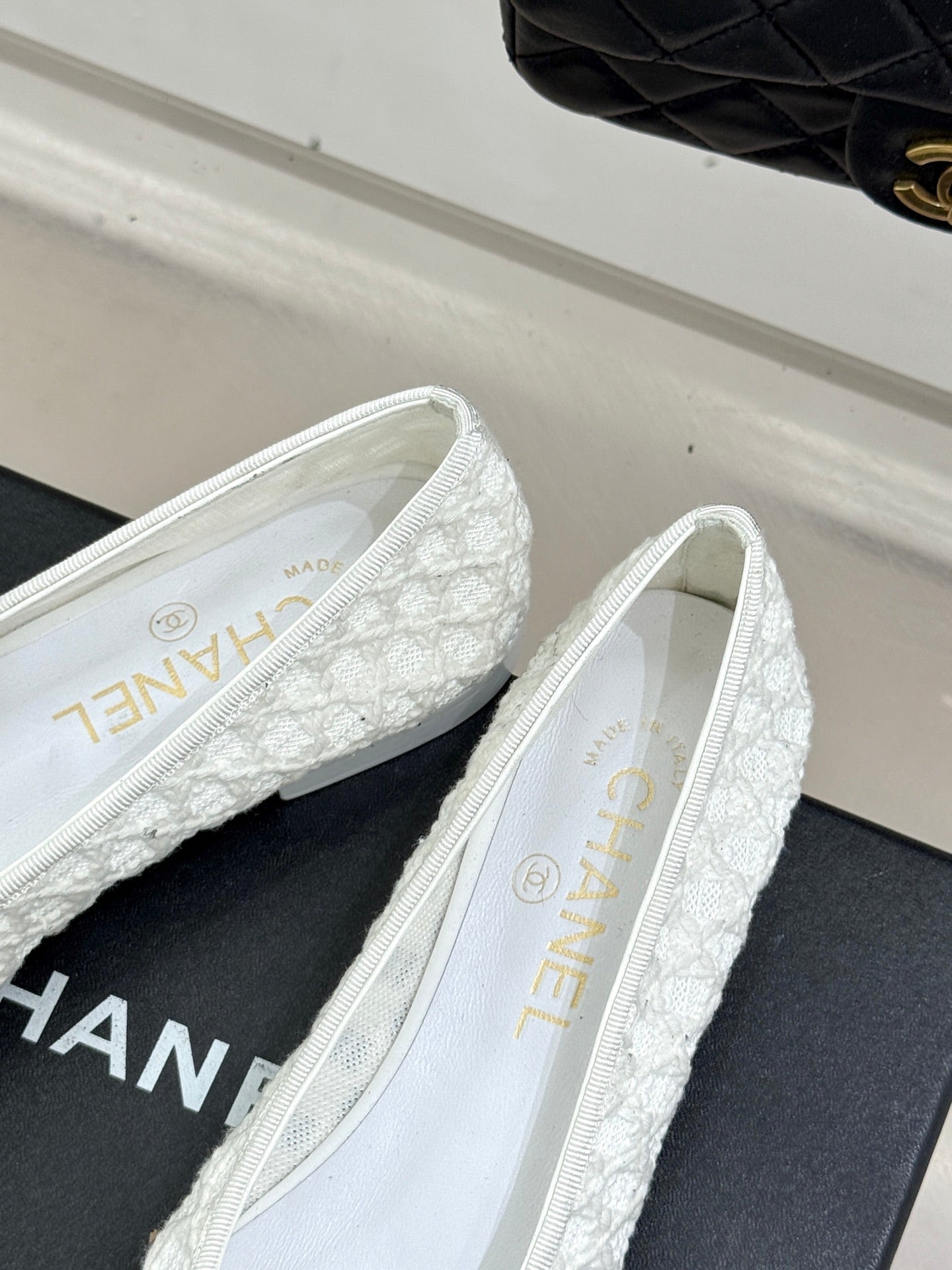 White lace ballet flats with black toe caps and CC logo, side view on shoebox