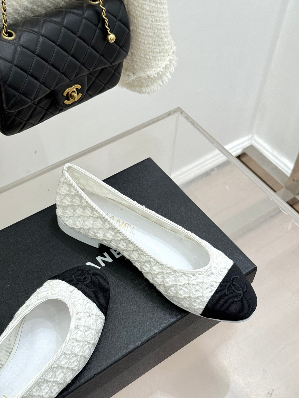 White lace ballet flats with black toe caps and CC emblem, shown on shoebox