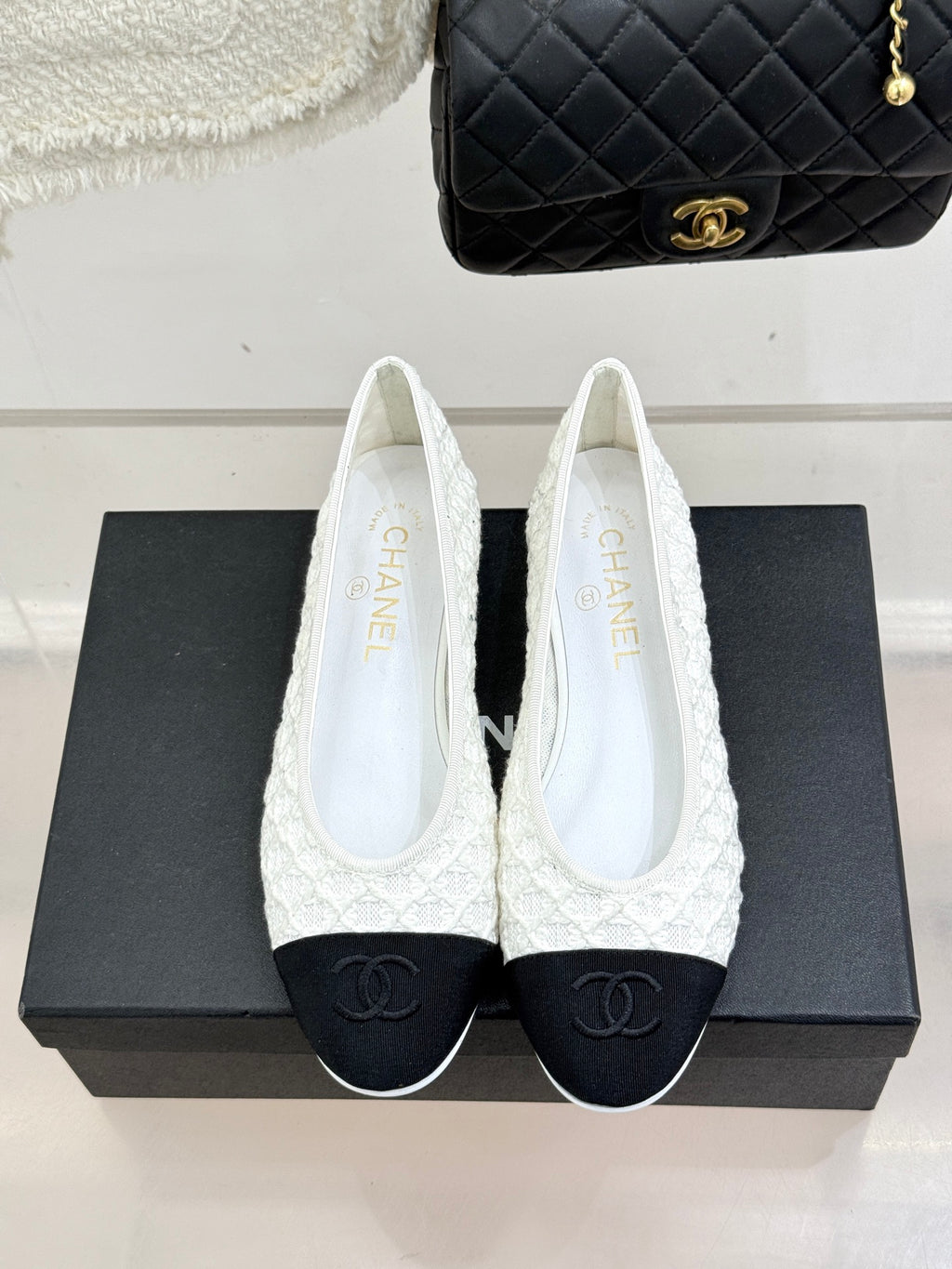 White lace ballet flats with black toe caps and CC logo, front view on shoebox
