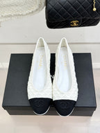 White lace ballet flats with black toe caps and CC logo, front view on shoebox