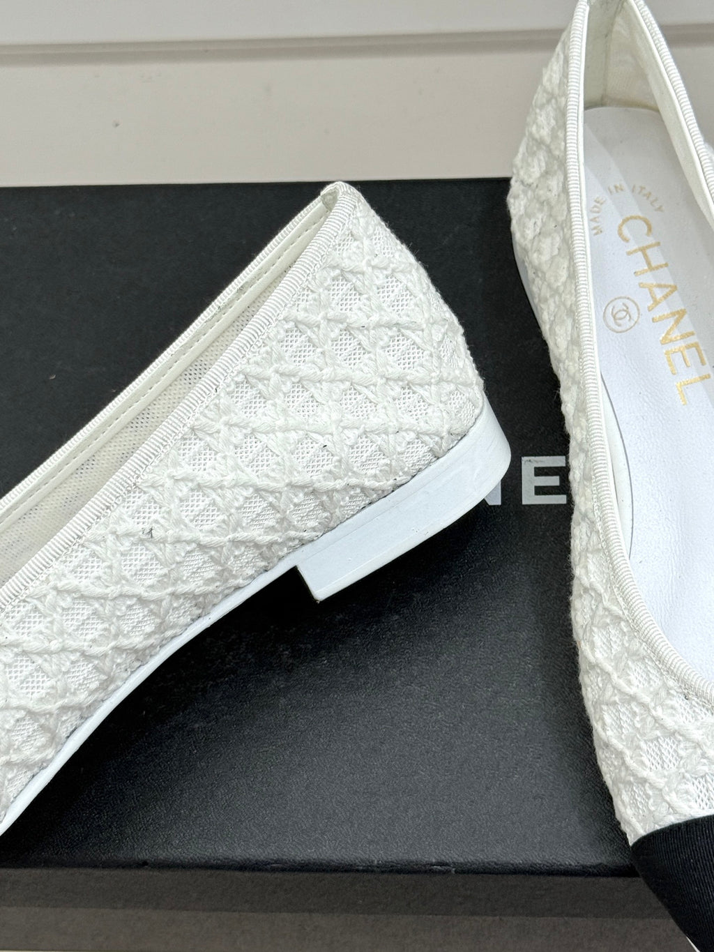 White lace ballet flat with textured vamp and black toe cap, on shoebox