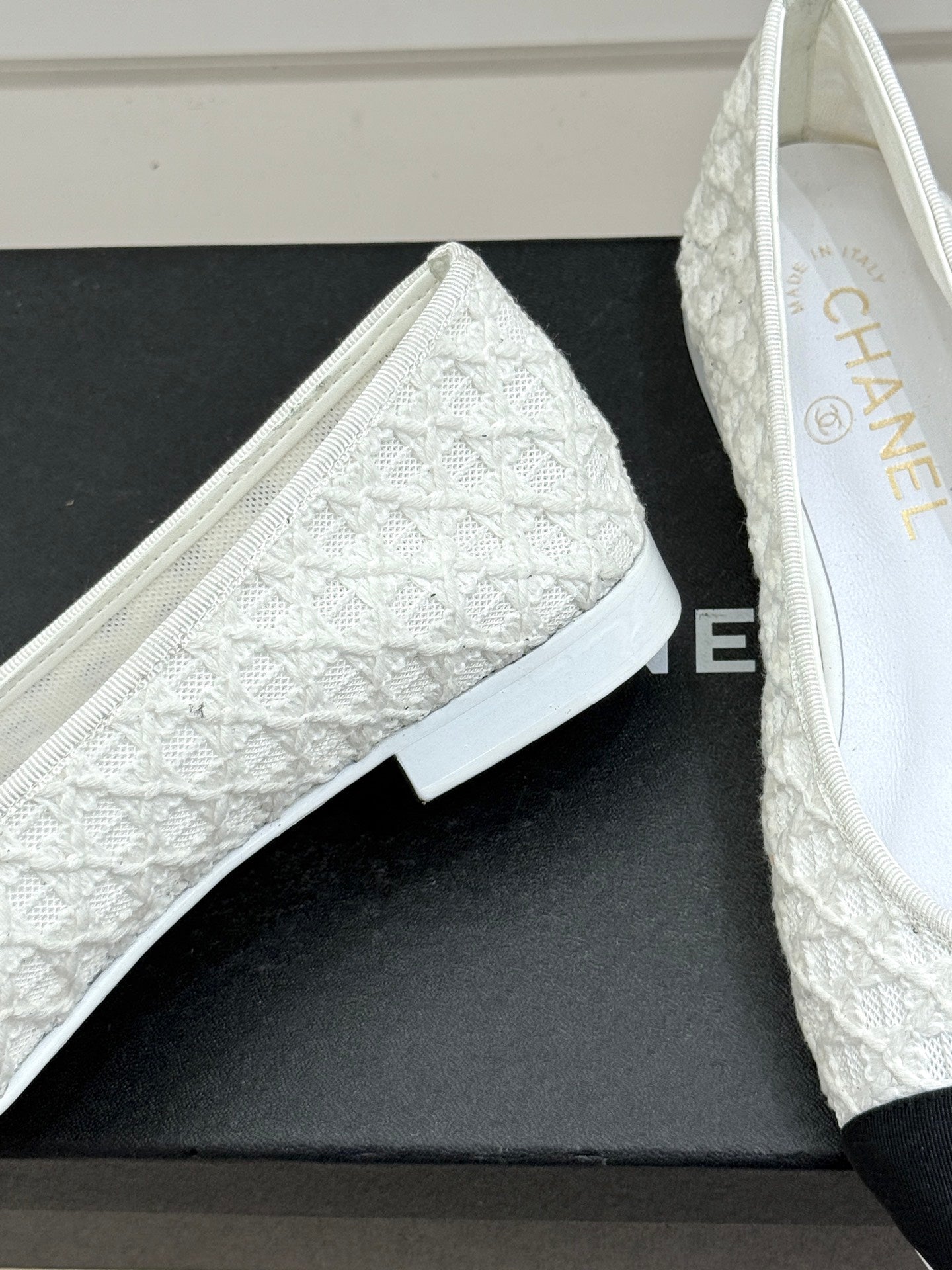 White lace ballet flat with textured vamp and black toe cap, on shoebox