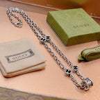 Silver-toned charm necklace with black enamel quatrefoil motifs and toggle clasp