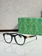 Black eyeglass frames with clear lenses and gold-tone logo detail on the temple