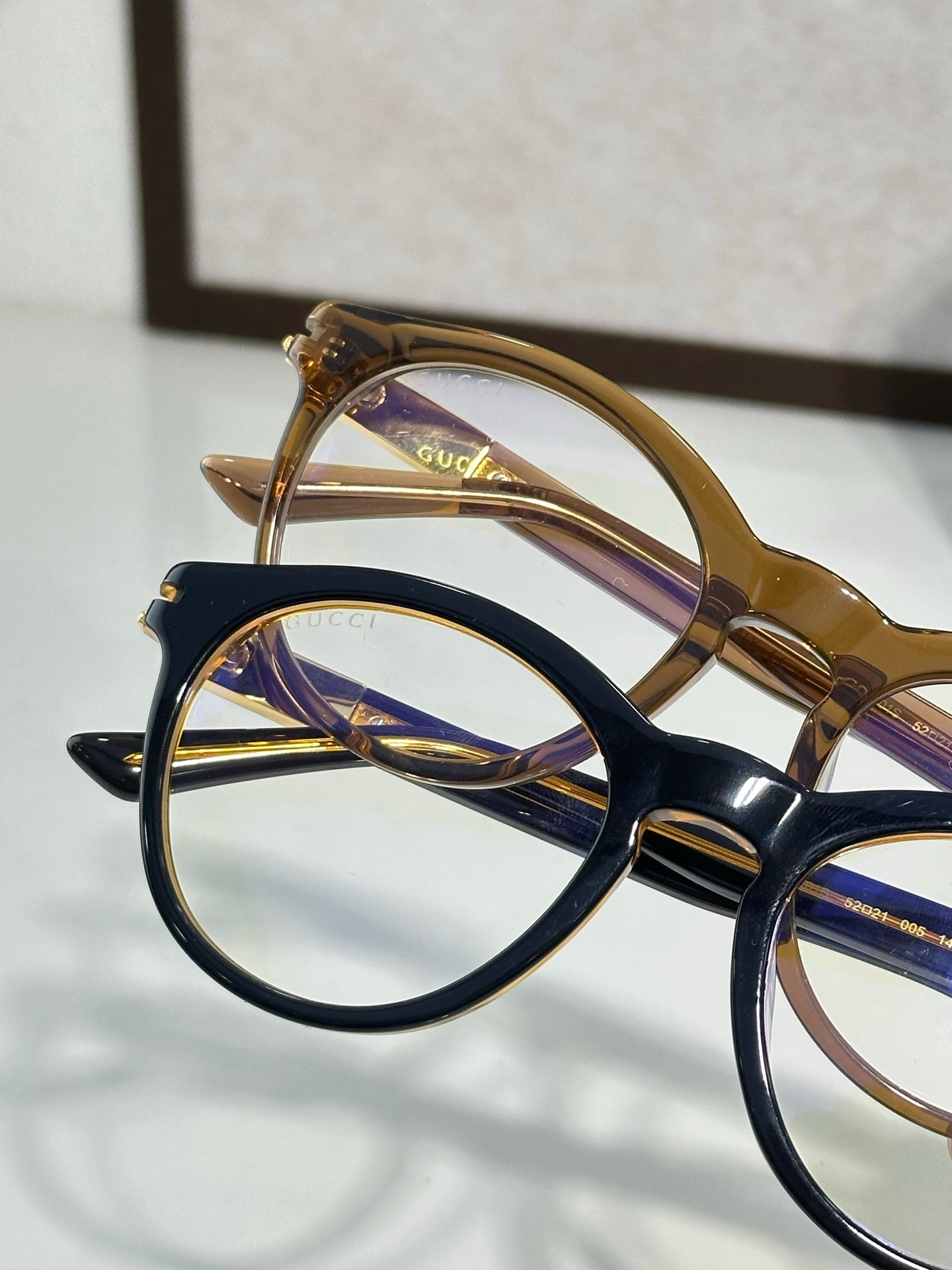 Gold-brown and black eyeglass frames overlapping, clear lenses visible