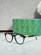 Black eyeglass frames with clear lenses and gold-tone temple logo, side view