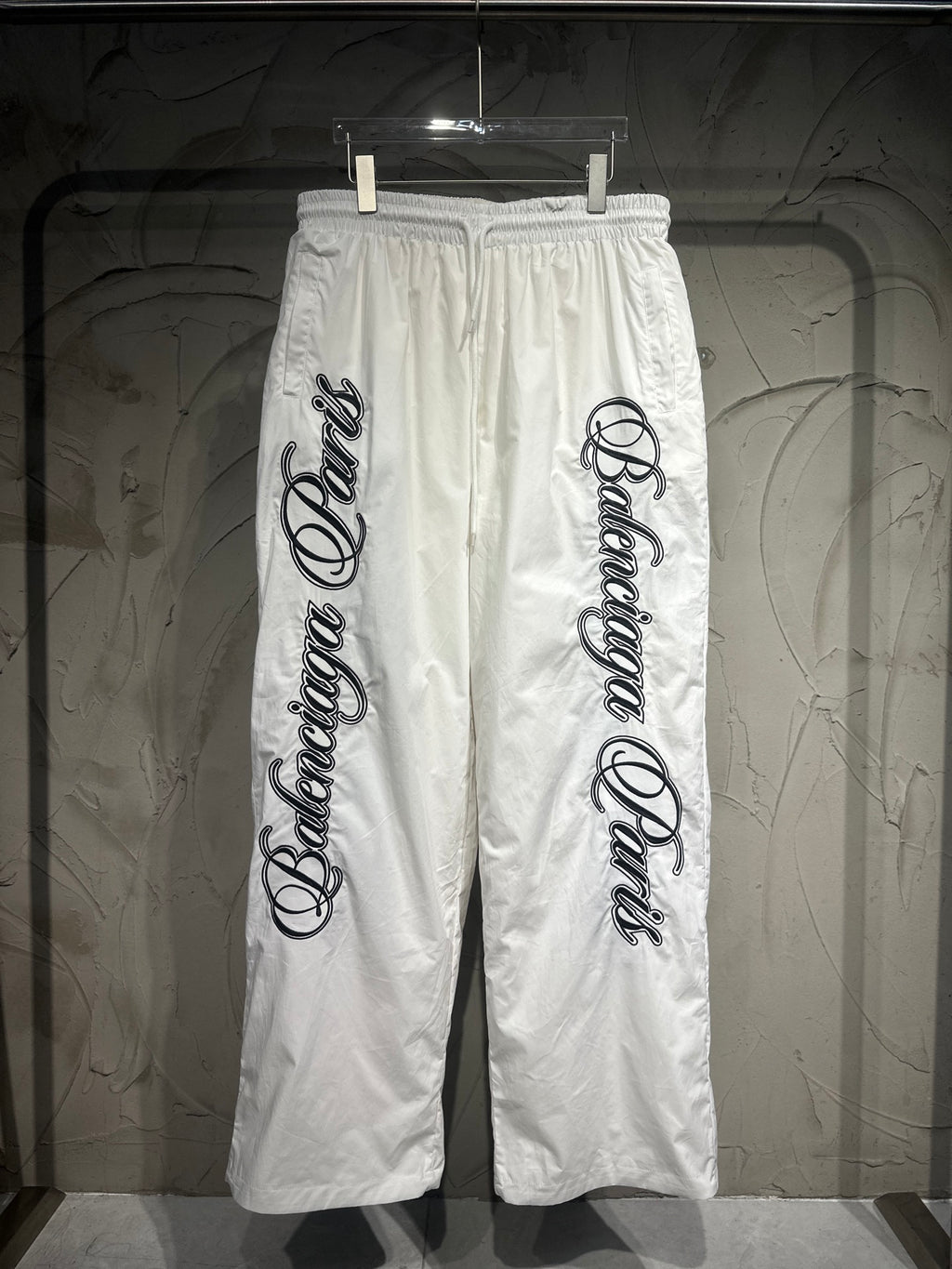 White track pants with elastic waistband, drawstring, and large vertical logo print