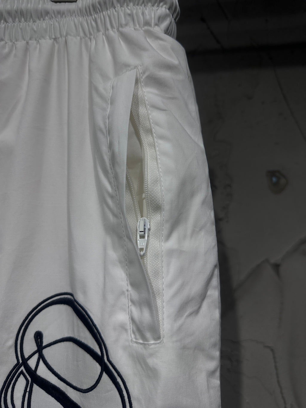 White track pants with front zip pocket and drawstring, elastic waist