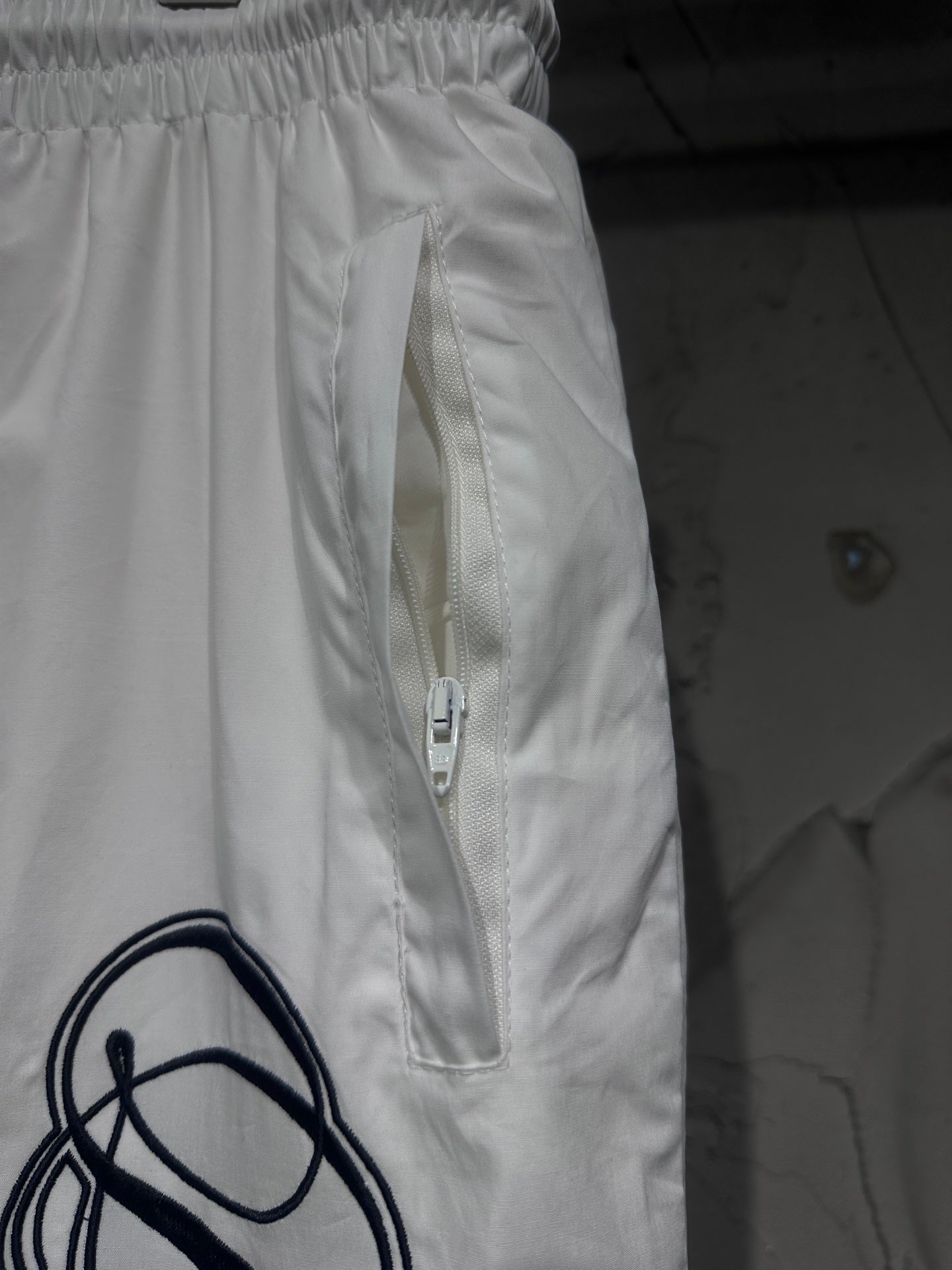 White track pants with front zip pocket and drawstring, elastic waist