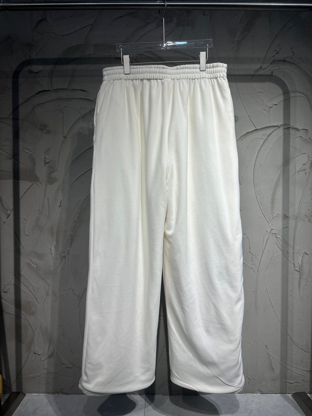 White track pants hanging on a hanger, elastic waistband and wide straight legs