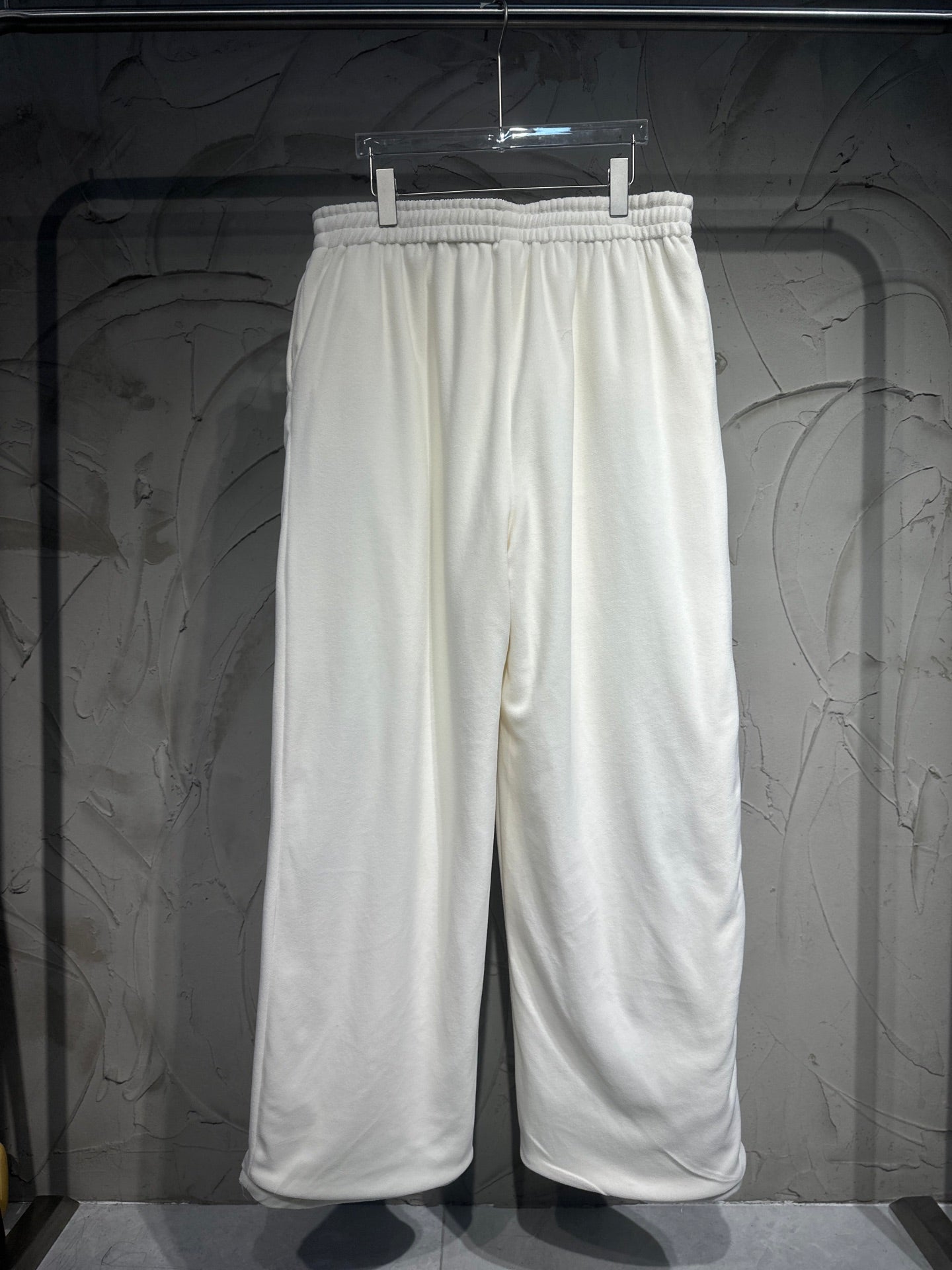 White track pants hanging on a hanger, elastic waistband and wide straight legs