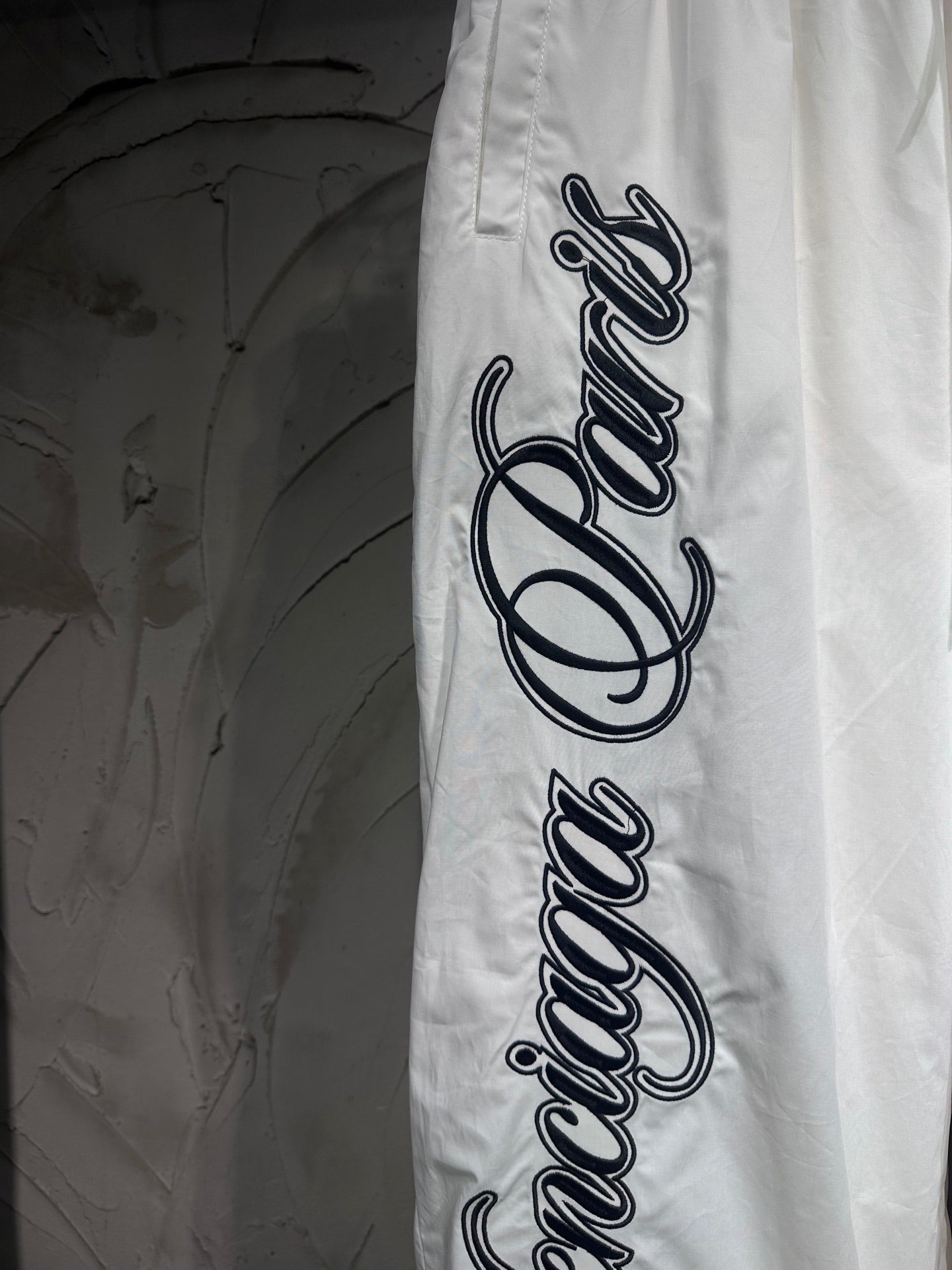 White track pants with oversized black logo lettering along the outer leg