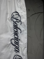 White track pants featuring a large vertical black script logo on the leg