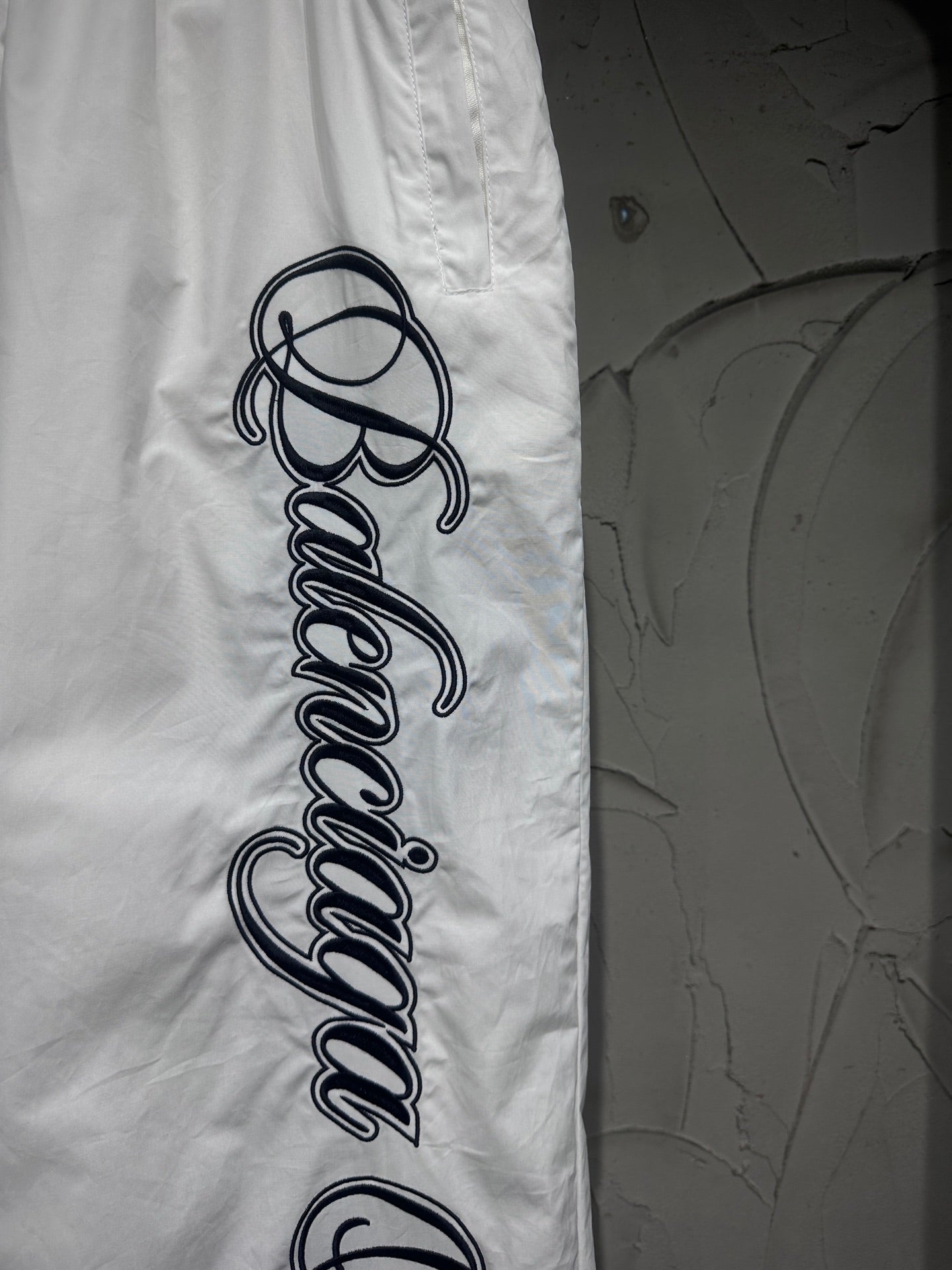 White track pants featuring a large vertical black script logo on the leg