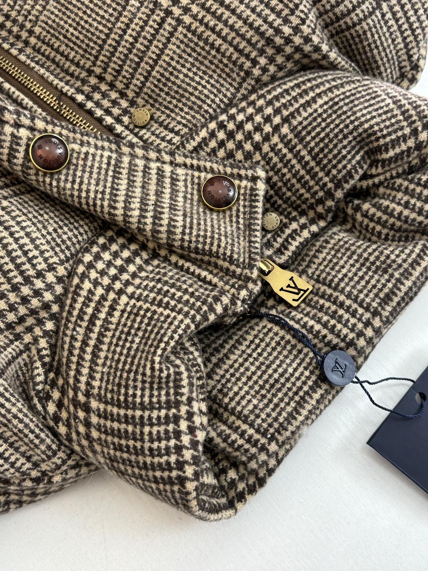 Houndstooth jacket close-up with zipper, snap buttons, and small logo tag