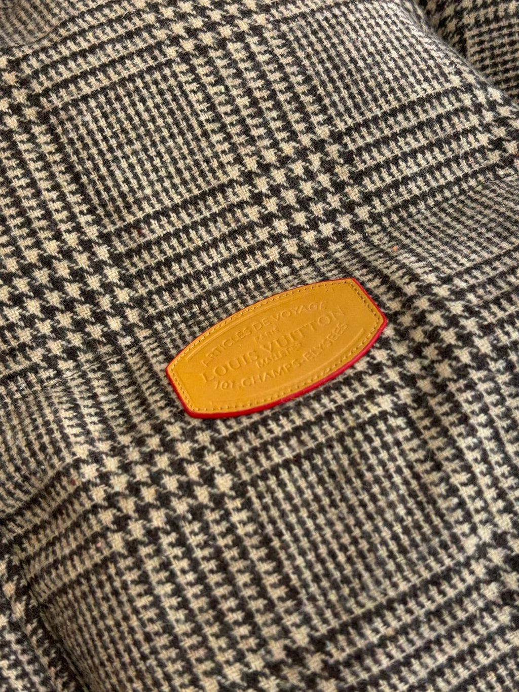 Close-up of houndstooth jacket fabric with orange Louis Vuitton logo patch