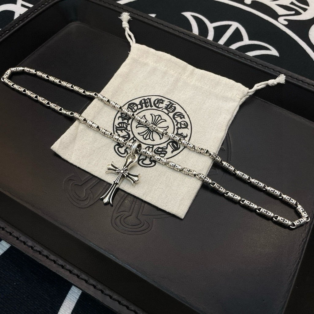 Silver-tone cross pendant necklace with textured link chain laid on a storage pouch.