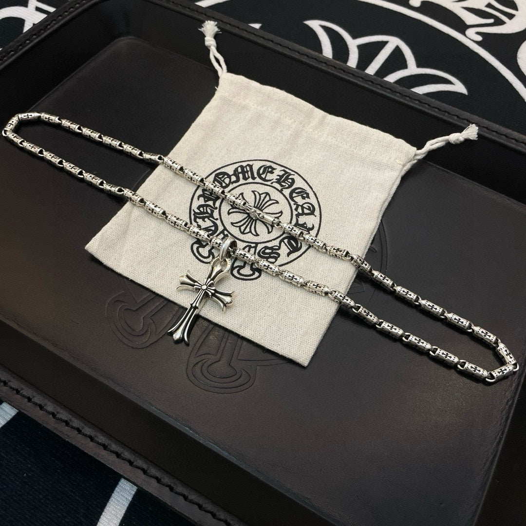 Silver-tone cross pendant necklace with textured link chain laid on a storage pouch.