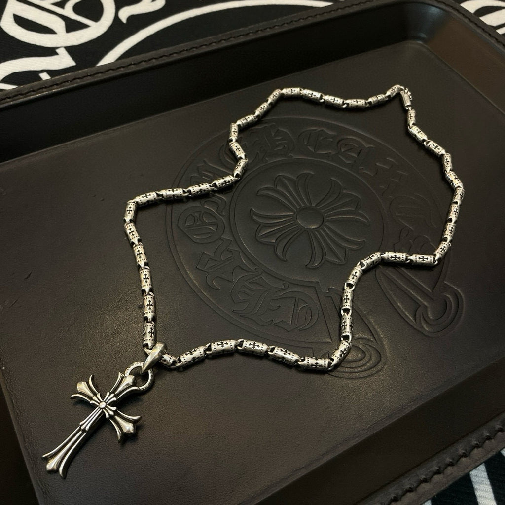 Silver-tone cross pendant necklace with textured link chain on a display tray.