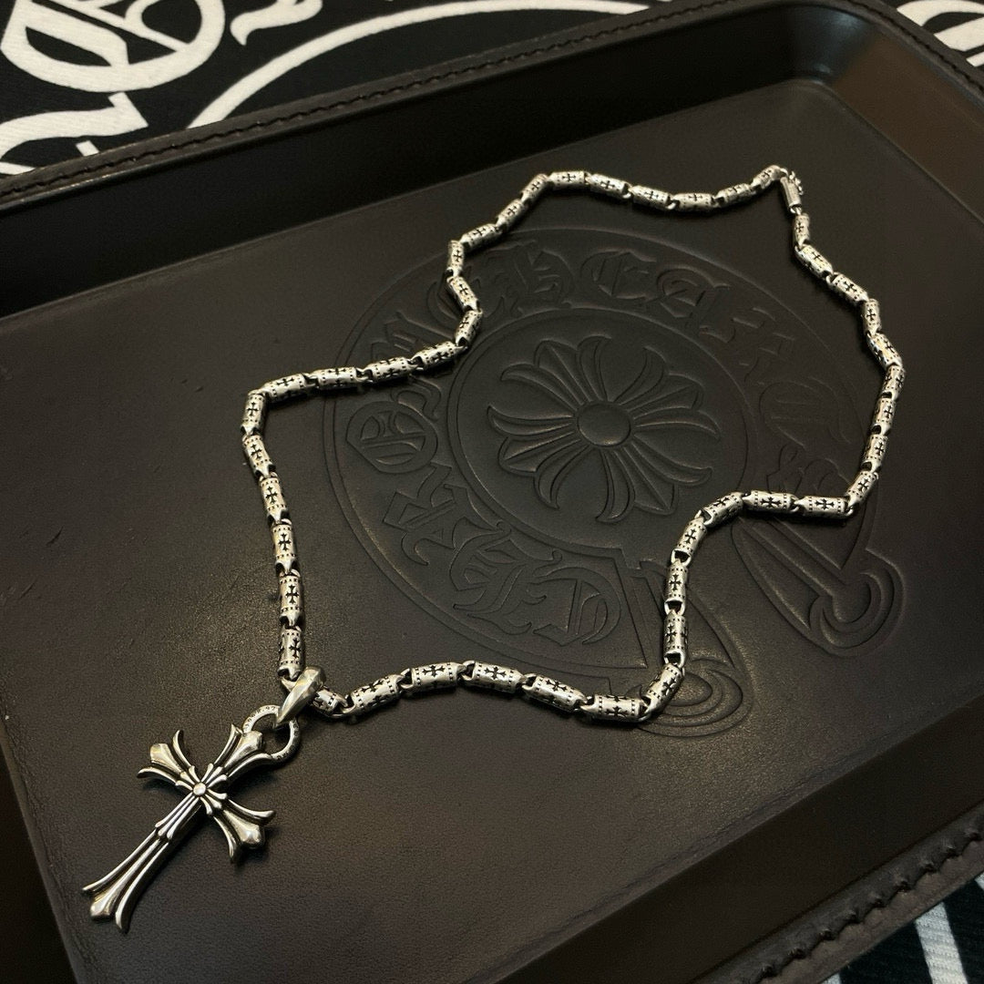 Silver-tone cross pendant necklace with textured link chain on a display tray.