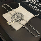 Silver chain necklace with circular pendant and heart-shaped cross charm on pouch