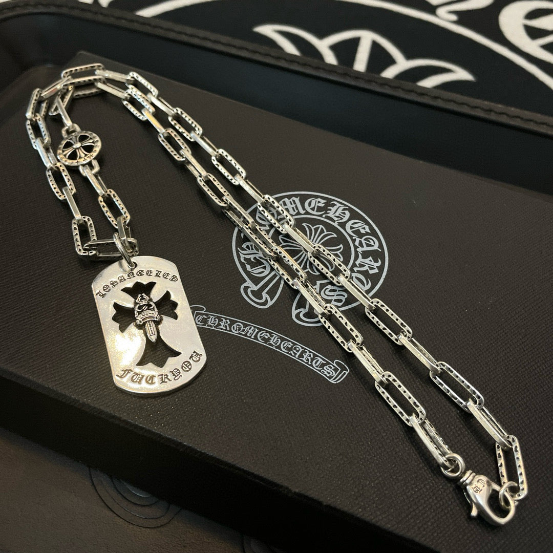Silver charm necklace on tray with dog-tag pendant and compass-style charm