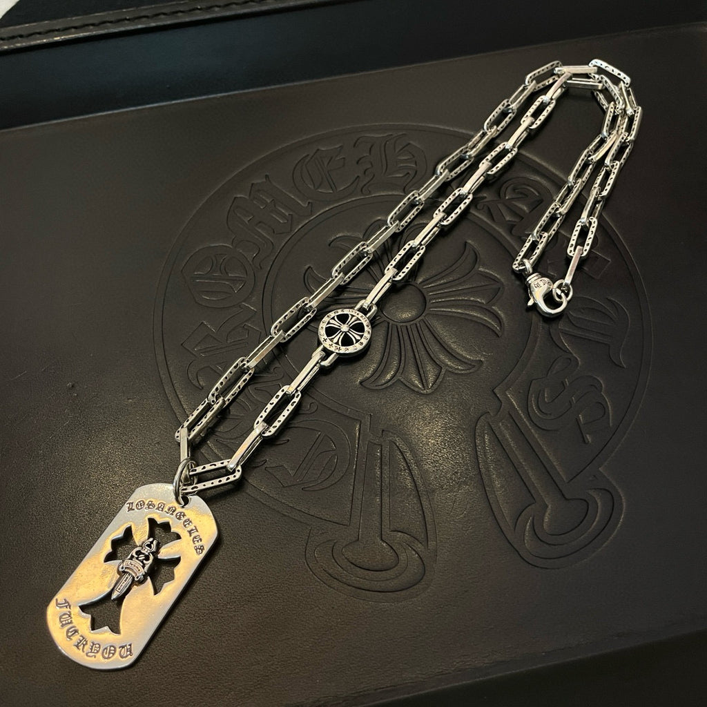 Silver chain necklace laid on leather with circular pendant and flower emblem charm