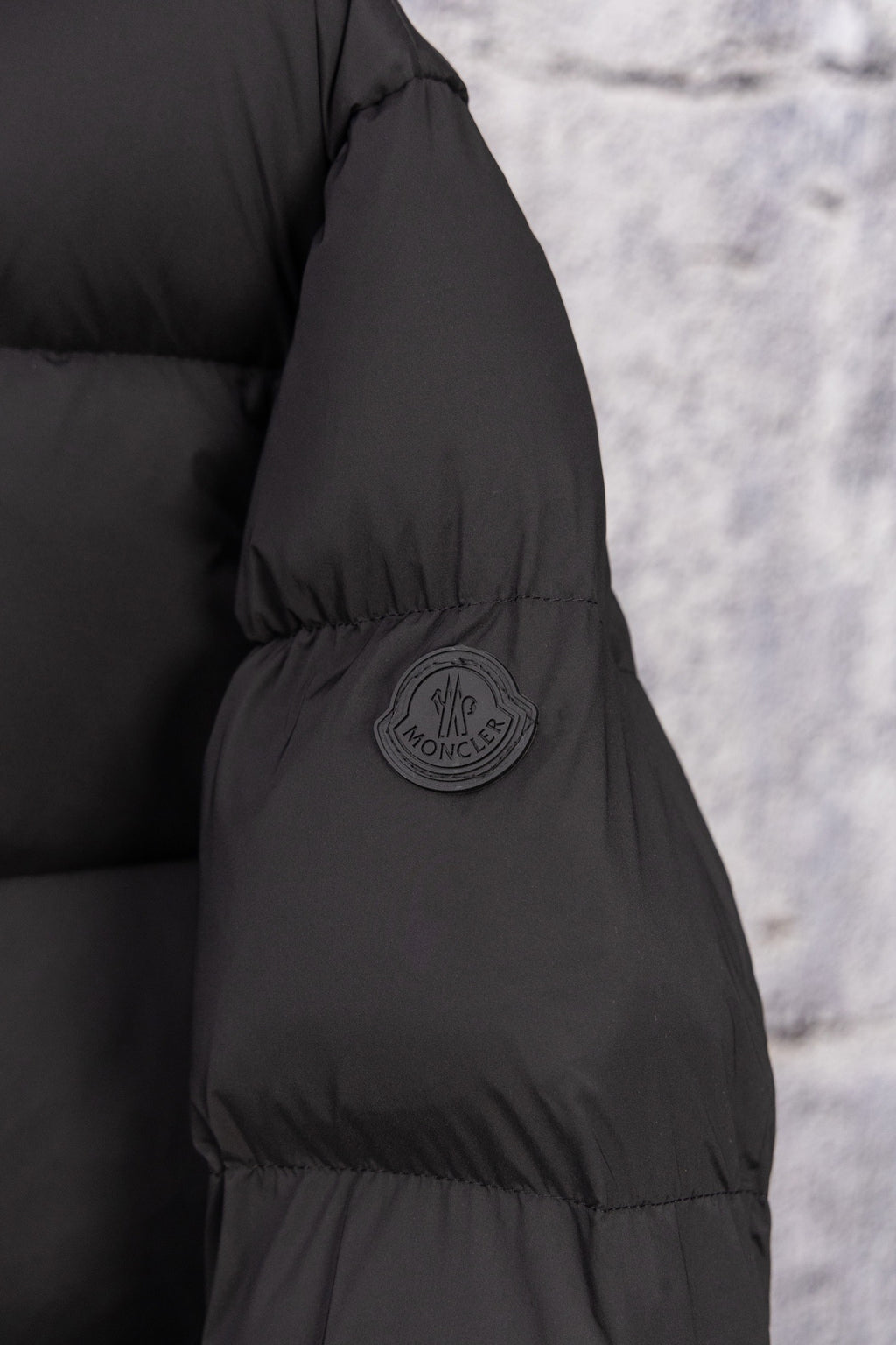 Dark puffer coat sleeve with round logo patch and quilted paneling