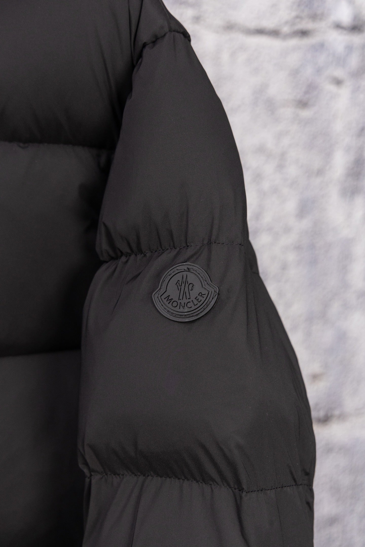 Dark puffer coat sleeve with round logo patch and quilted paneling