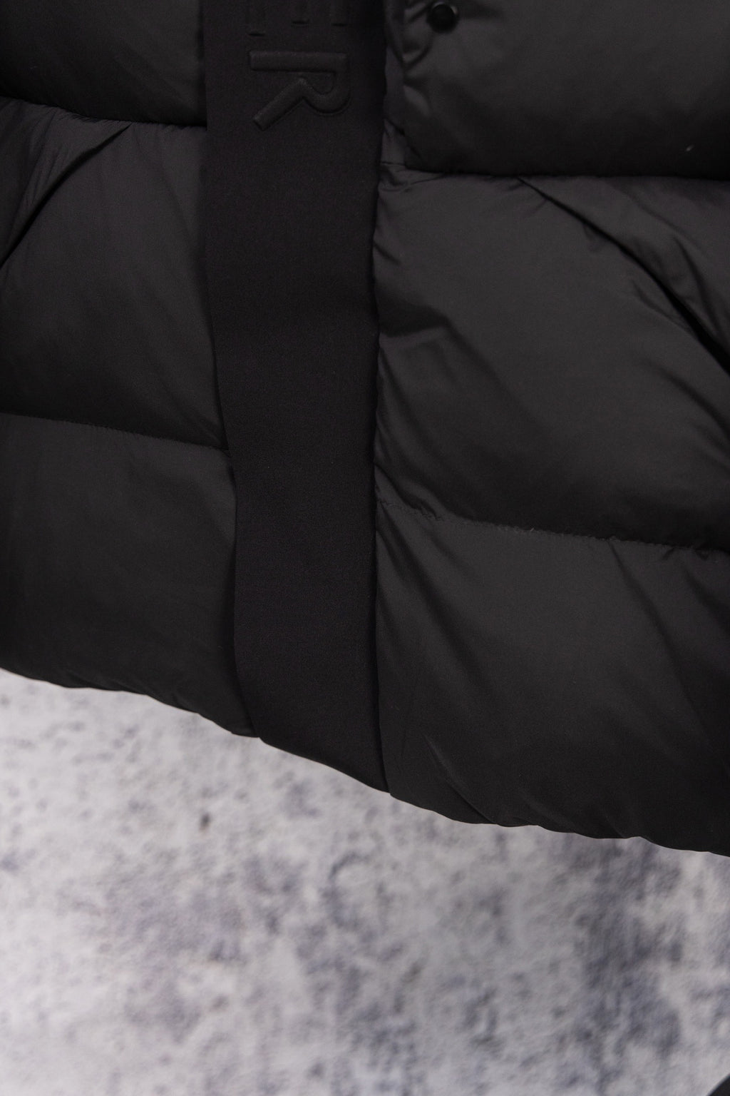 Dark long puffer coat front with snap buttons and quilted lower panel