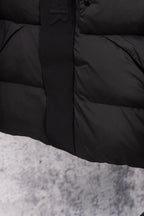 Dark long puffer coat front with snap buttons and quilted lower panel