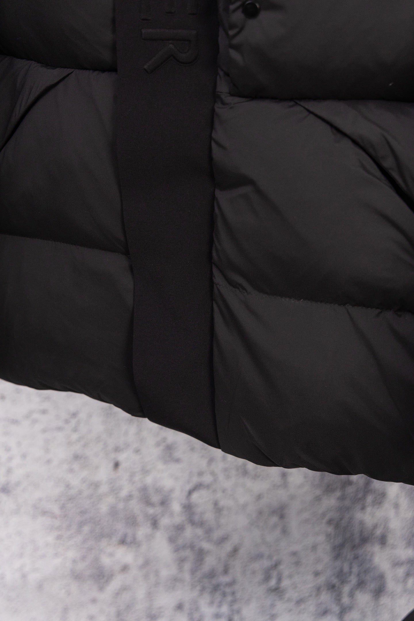 Dark long puffer coat front with snap buttons and quilted lower panel