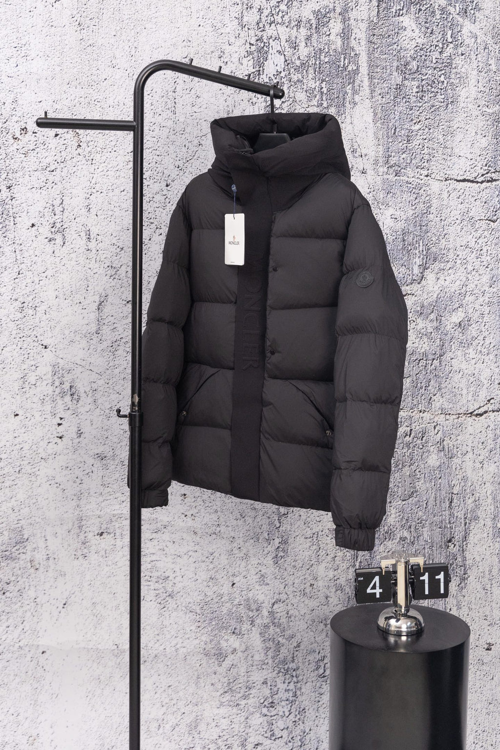 Moncler long hooded puffer jacket, dark, front view on wall display with zip