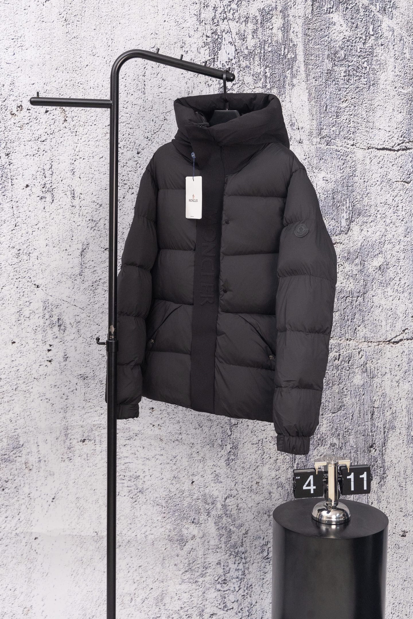 Moncler long hooded puffer jacket, dark, front view on wall display with zip