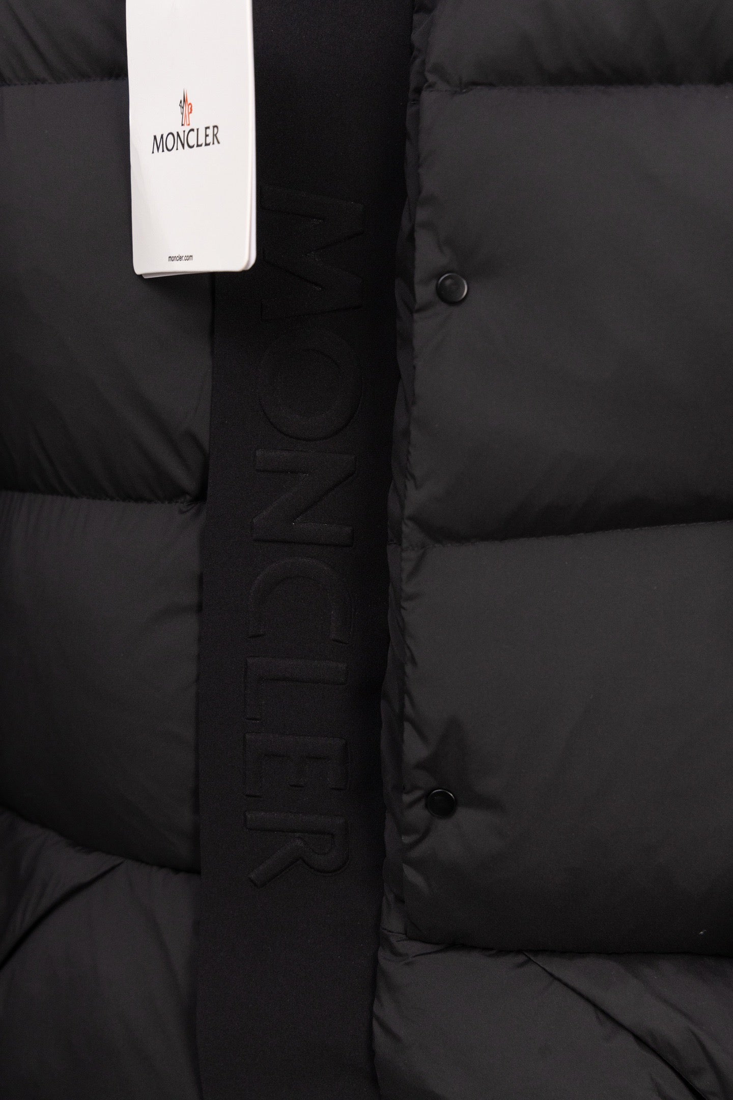 Dark puffer coat with vertical MONCLER lettering strip and front snap buttons