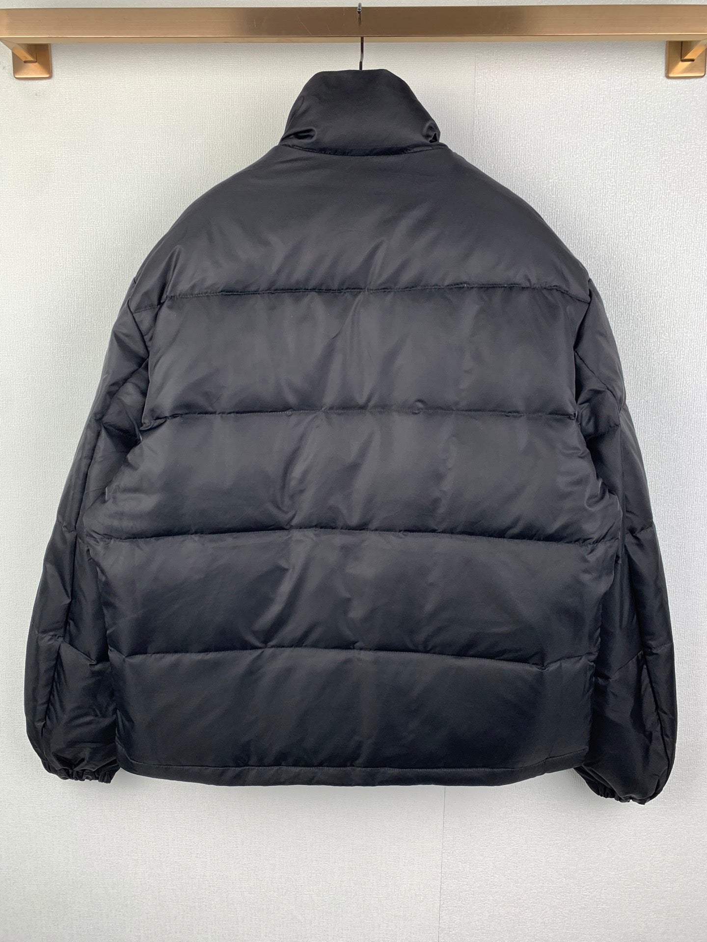 Dark puffer jacket back view with horizontal quilted panels and high neck