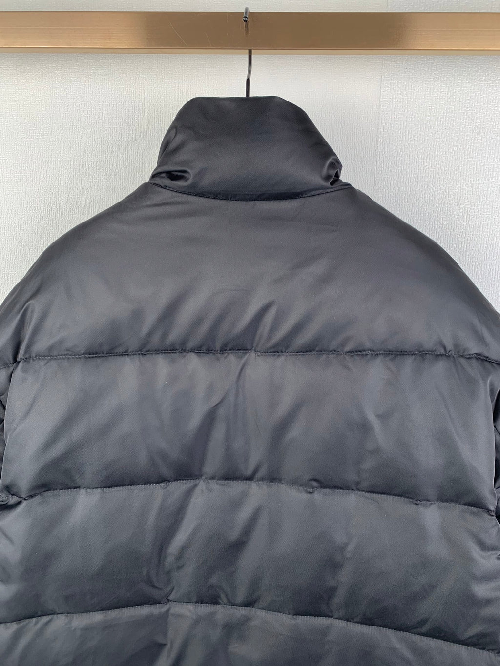 Dark puffer jacket back view with quilted stripes and raised collar