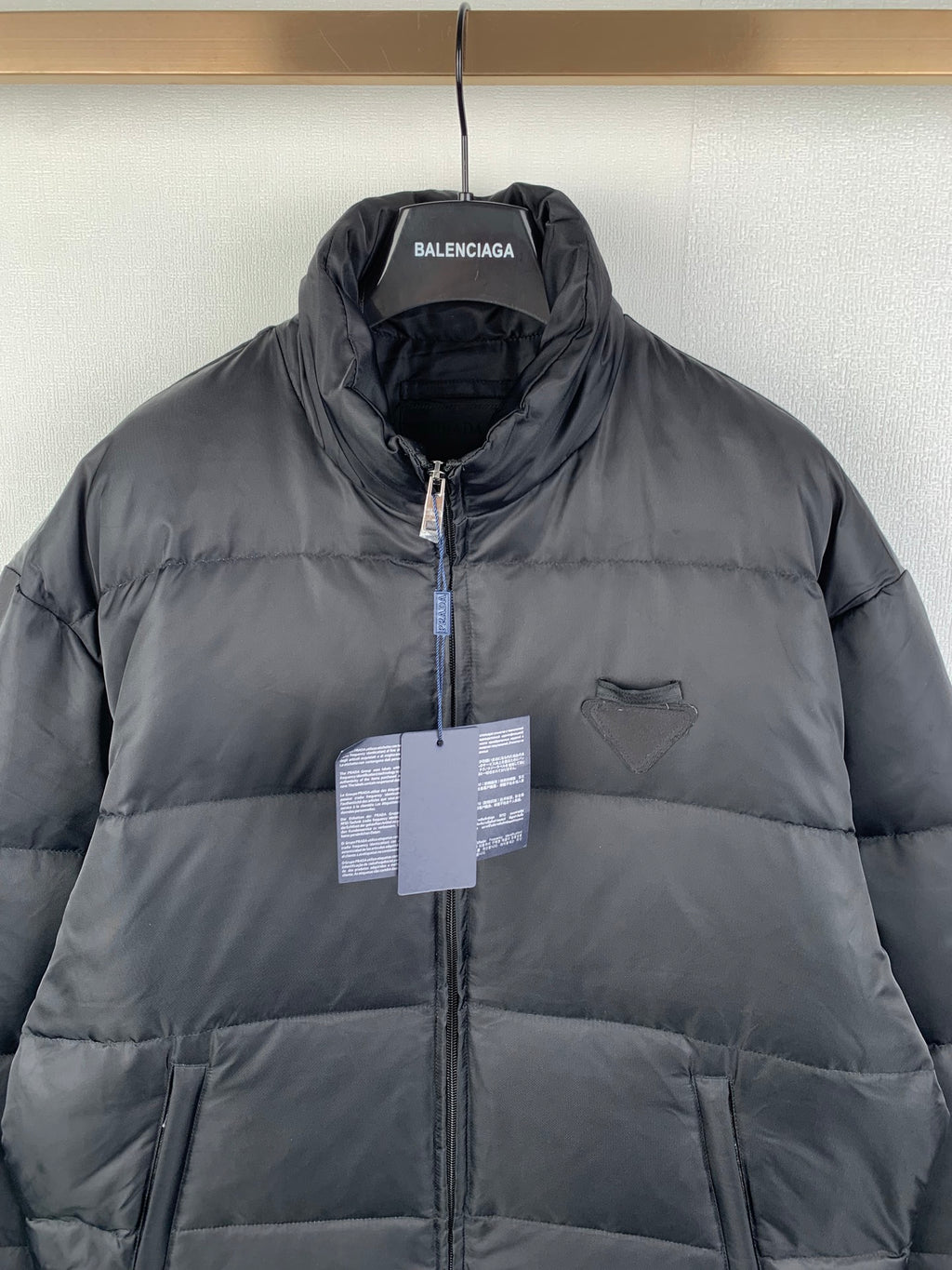 Dark puffer jacket with full-zip front, stand collar, and BALENCIAGA hang tag