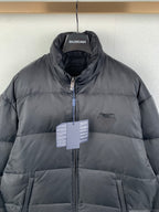 Dark puffer jacket with full-zip front, stand collar, and BALENCIAGA hang tag