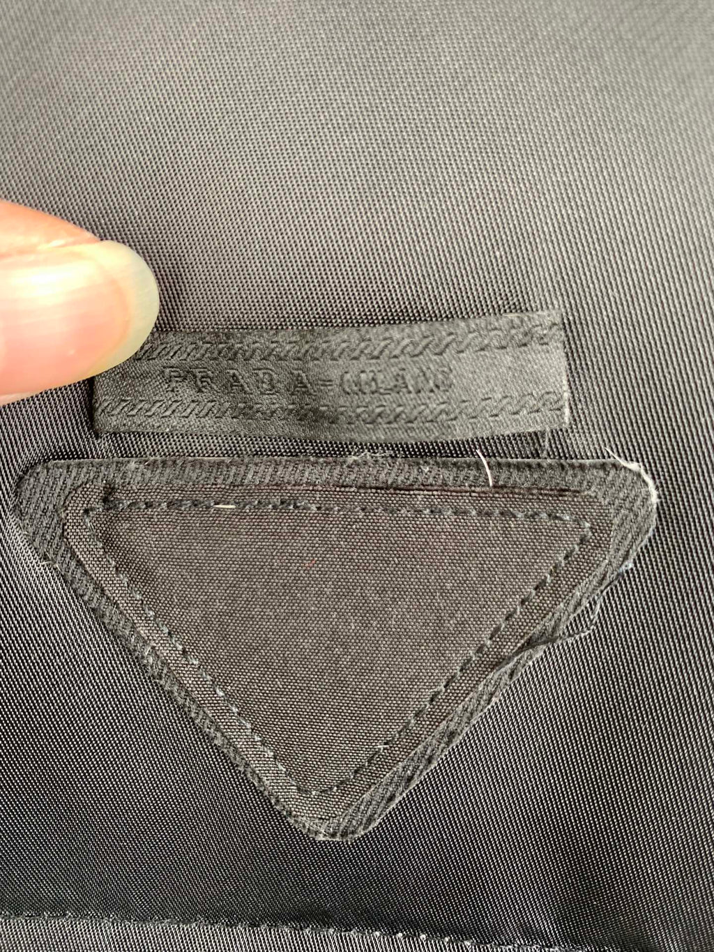 Gray fabric label with stitched triangular emblem and PRADA text