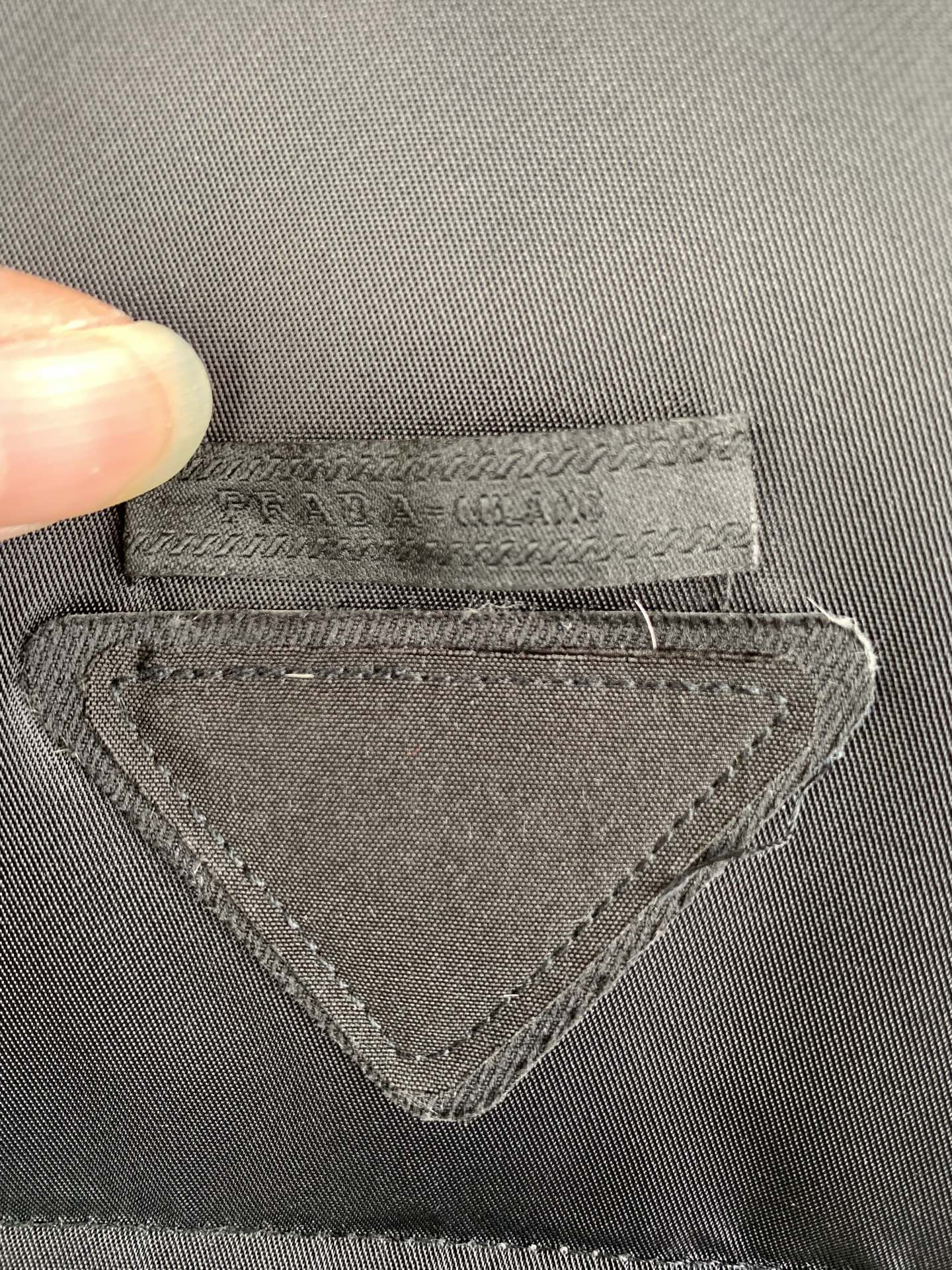 Gray fabric label with stitched triangular emblem and PRADA text