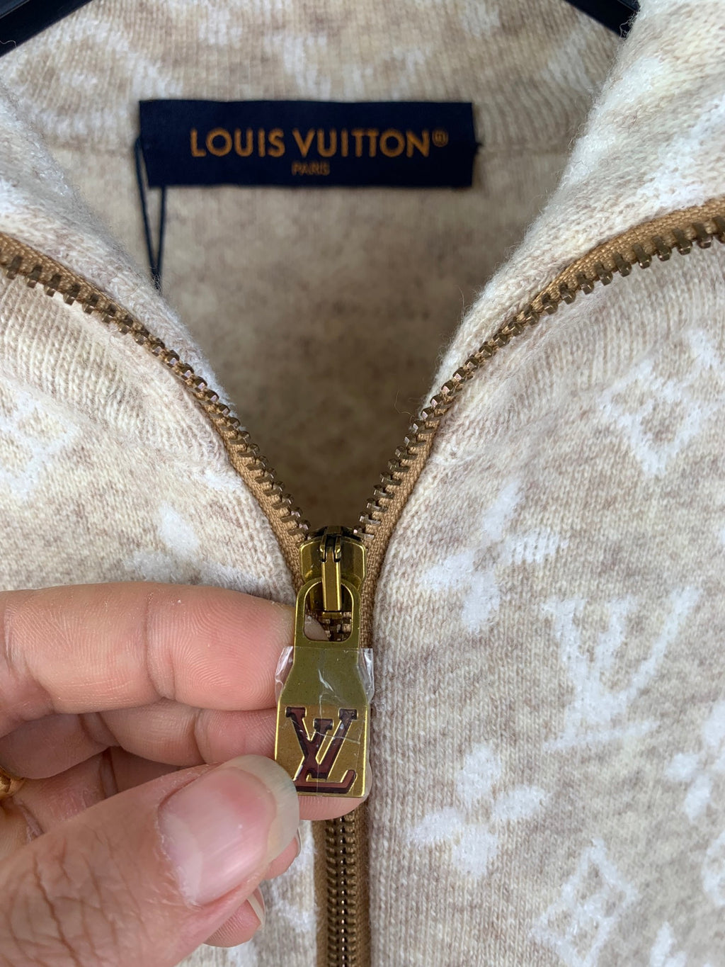 Close-up of gold-tone zipper pull and monogram zip tab on beige sweater