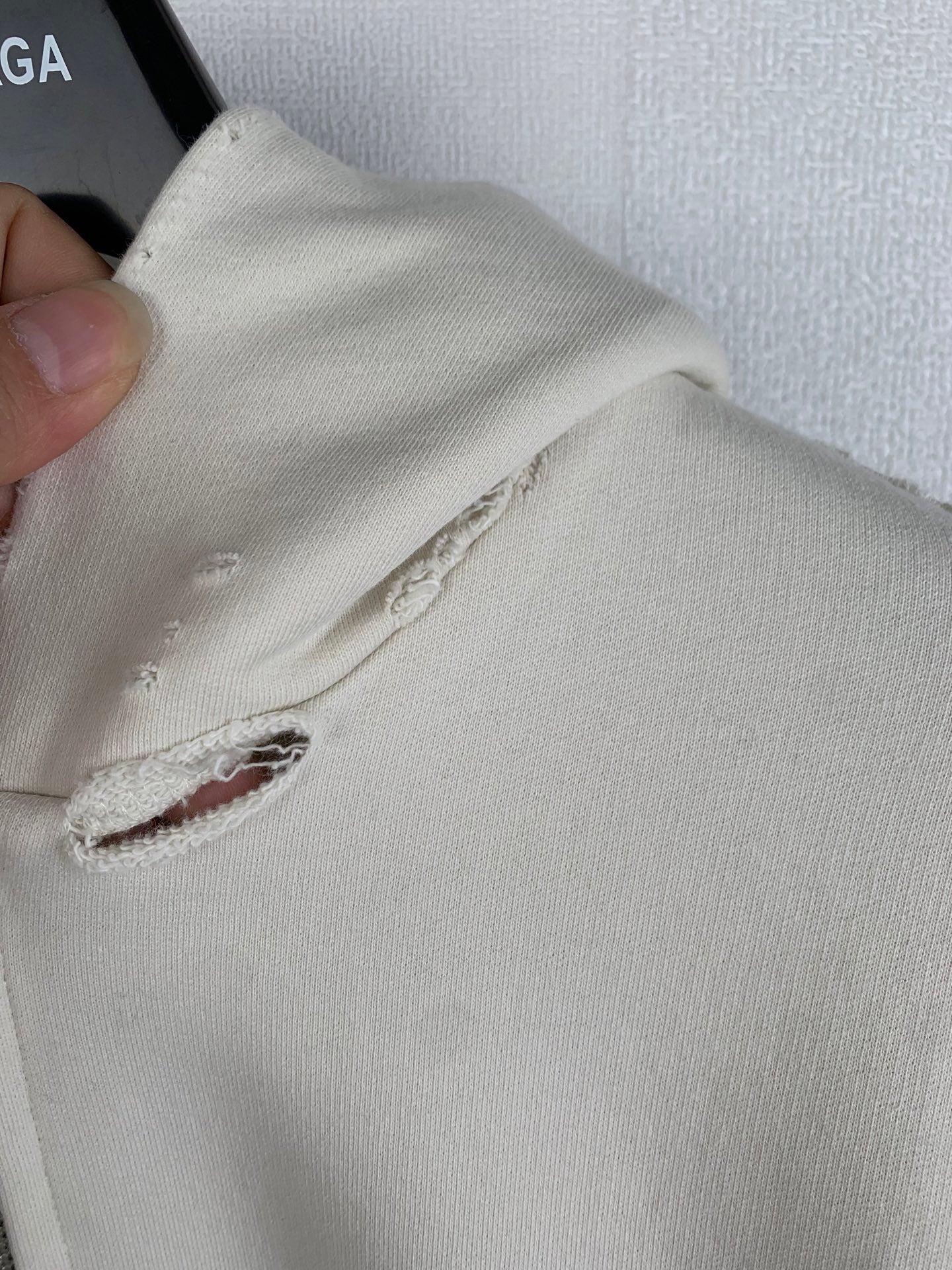 Cream hoodie sleeve with small frayed hole and stitched seam detail
