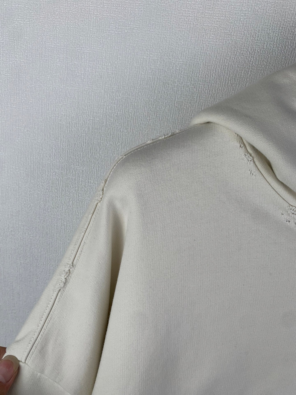 Cream hoodie side panel with stitched seam and slight fraying near shoulder